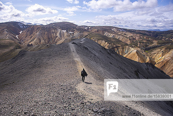 Mann mit Kap  der einen Pfad auf dem Gipfel eines Berges in Island hinuntergeht