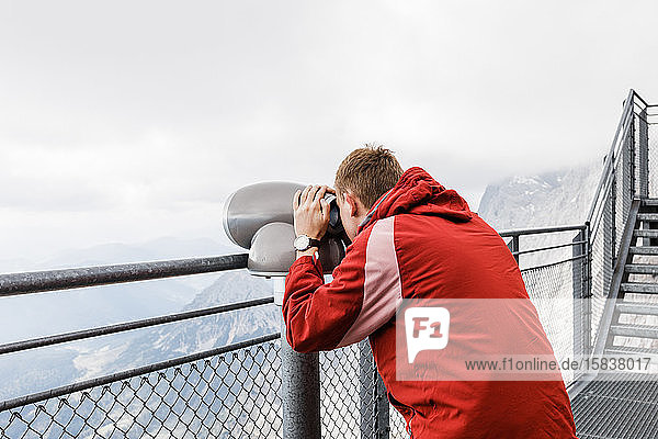 junger blonder Mann schaut aus der Beobachtung mit dem Fernglas auf Bergansichten