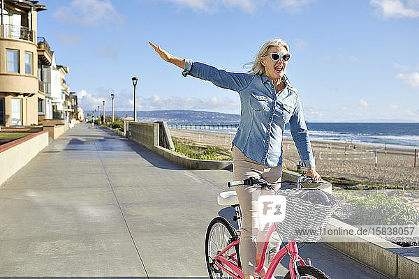 Fröhliche ältere Frau mit Sonnenbrille fährt Fahrrad auf der Straße gegen den Himmel in der Stadt