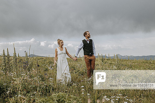 Braut und Bräutigam spazieren durch ein Feld mit Wildblumen in Wyoming