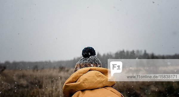 der Rücken einer Pudelmütze an einem Kind  das draussen im Schnee spielt