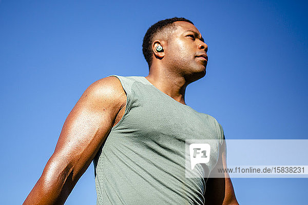 Porträt der oberen Hälfte eines starken Athleten vor blauem Himmel