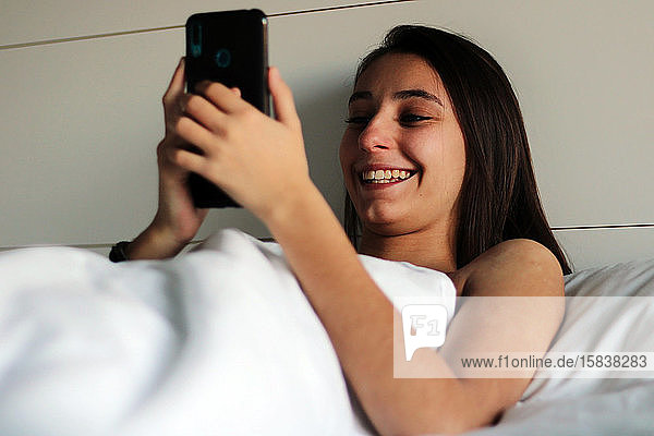 Ein junges und hübsches Mädchen ist gerade mit dem Handy im Bett aufgewacht.