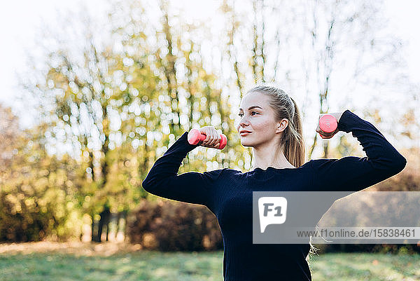 Beautiful young girl posing with dumbbell  outdoors  looking away.
