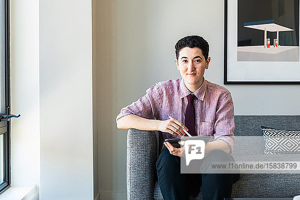 Porträt eines selbstbewussten Geschäftsmannes mit Grafiktablett  der im Büro auf dem Sofa an der Wand sitzt