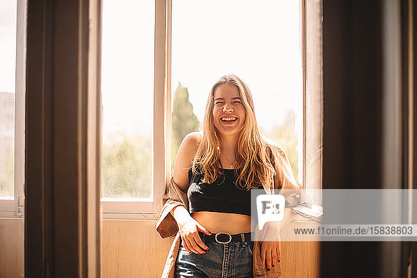 Fröhliche junge Frau lacht  während sie im Sommer auf dem Balkon steht