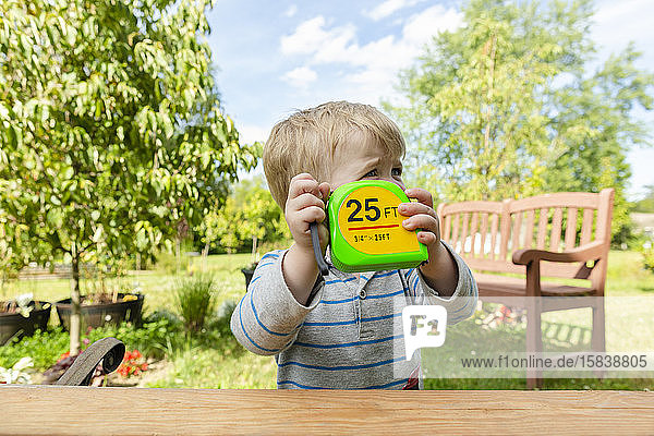 Kleiner Junge hält Maßband hoch  während er draußen im Garten misst