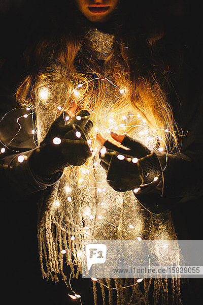 Junge Frau hält Weihnachtsbeleuchtung im Dunkeln im Freien
