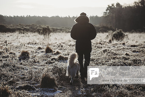 Rückansicht eines Mannes  der an einem kalten  frostigen Morgen mit seinem Hund über die Heide spaziert