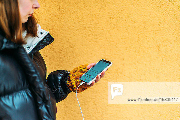 Junge Frau benutzt Smartphone  während sie an gelber Wand steht
