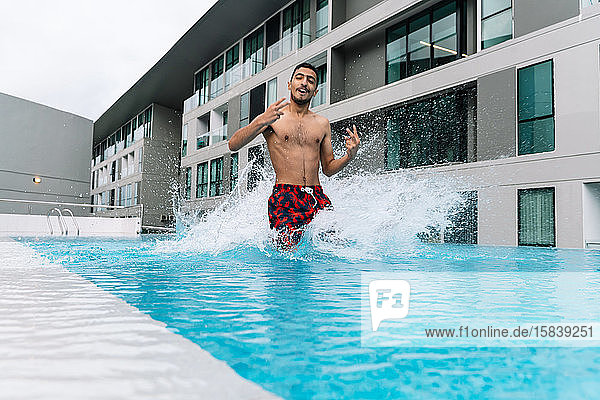 Junger Mann springt in einen von Gebäuden umgebenen Pool
