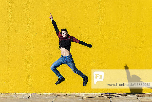 Lächelnder junger Teenager springt an einem sonnigen Tag gegen die gelbe Wand