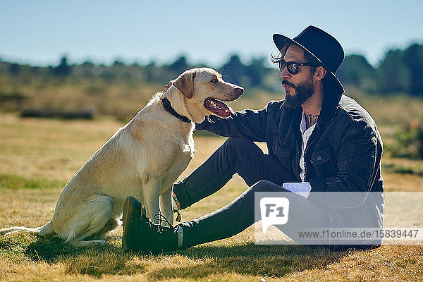 Porträt eines jungen tätowierten Mannes  der mit seinem Hund auf dem Land spielt