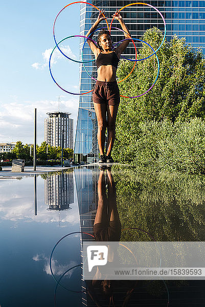 Young woman performing Hula Hoop dance with five rings in urban area