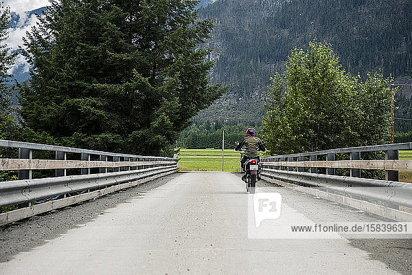 Eine Frau fährt an einem bewölkten Sommertag mit ihrem Motorrad über eine Brücke.