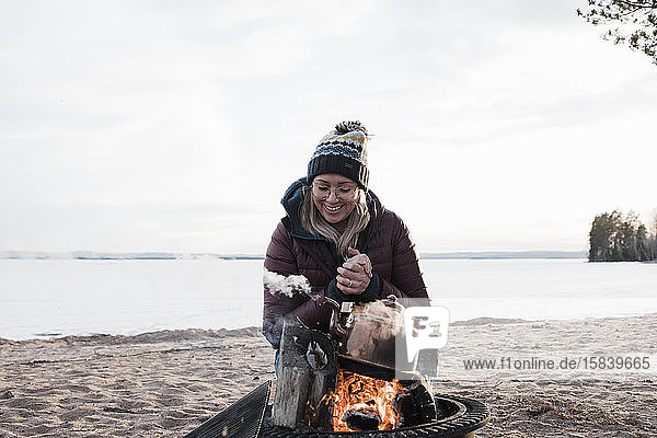 Frau  die sich im Winter am Strand am Lagerfeuer wärmt und lächelt
