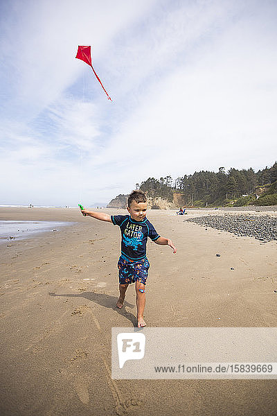 young boy running with kite on Oregon Coast beach.