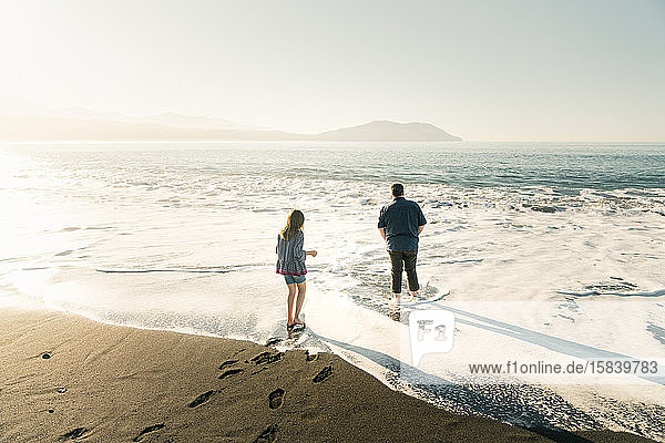 Father and daughter walking in water at the beach during sunset