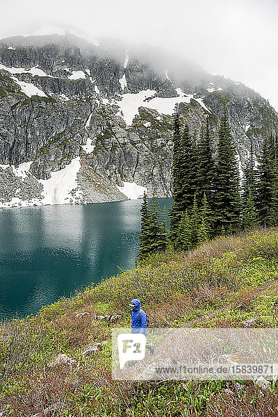 A woman hikes around a beautiful alpine lake on a cloudy  rainy summer day in the Coast Mountains around Pemberton  British Columbia.