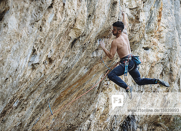 Ein Bergsteiger ohne Hemd schickt eine Sportkletterroute am spanischen Fels.