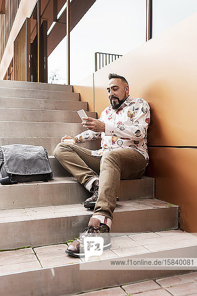 Gutaussehender junger Mann in legerer Kleidung  der mit seinem Handy Zeit im Freien verbringt