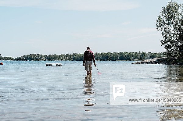 Mann  der im Sommer mit einem Fischernetz im Wasser steht