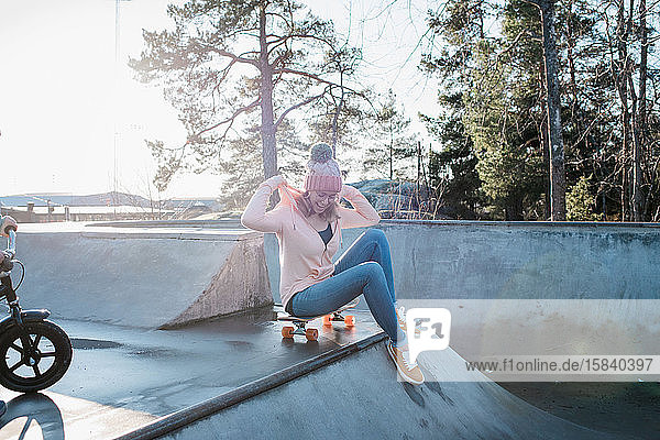 Frau saß auf einem Skateboard in einem Skatepark und lächelte in der Sonne