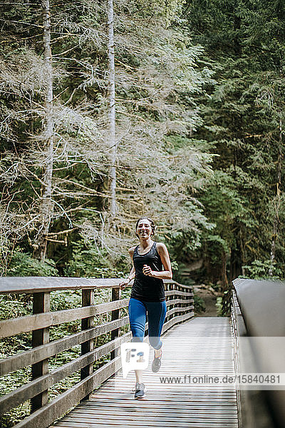 Eine fitte junge Frau joggt auf einer Brücke in einem Wald in Washington