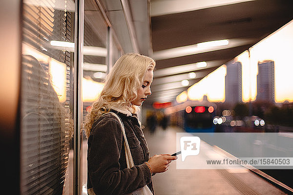 Young businesswoman using smart phone while waiting for subway train