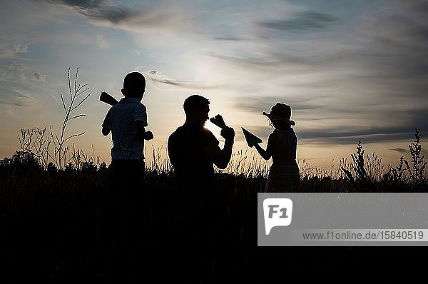 silhouette of father playing with son and daughter outside at sunset