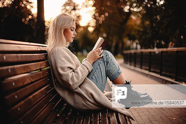 Teenager-Mädchen liest im Herbst auf einer Parkbank sitzend ein Buch