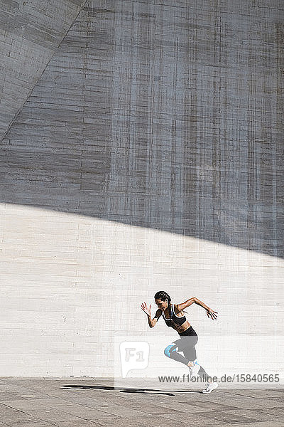 Pulled back view of female athlete running on concrete vertical