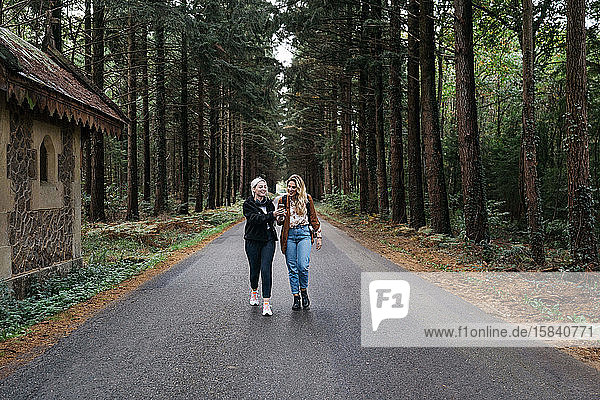 Zwei Frauen gehen auf einer Straße im Wald  während sie ihr Telefon beobachten