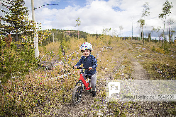 Young boy riding red bike on dirt pathway through forest.