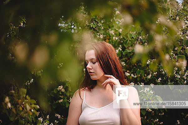 Junge Frau steht im Frühling inmitten blühender Zweige im Park