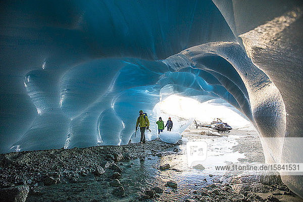 Drei Eiskletterer betreten eine Gletscherhöhle.
