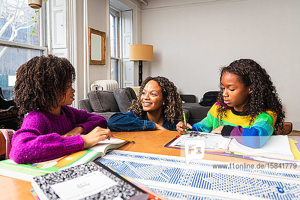 Lächelnde Mutter hilft Töchtern beim Lernen am Tisch im Wohnzimmer