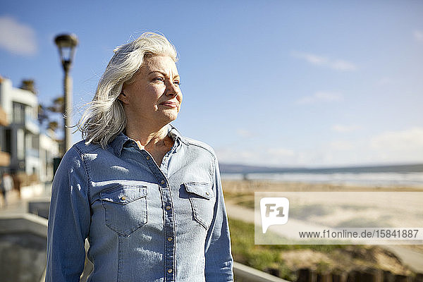Nachdenkliche ältere Frau steht bei Sonnenschein am Strand von Manhattan