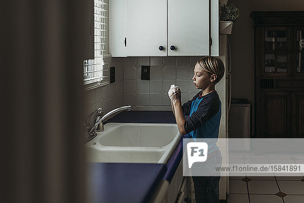 Seitenansicht eines Jungen im Schulalter beim Händewaschen am Spülbecken in der Küche