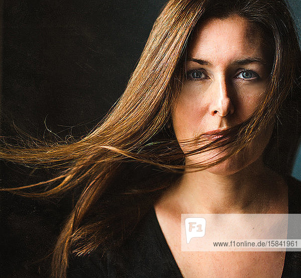 Bildnis einer Frau mit langen braunen Haaren  die über ihr Gesicht wehen.