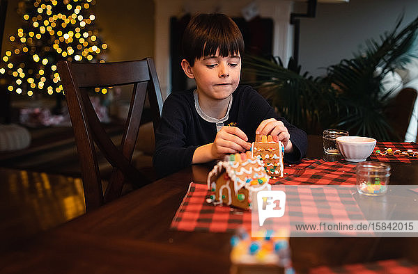Young boy decorating gingerbread house with candy at Christmas.