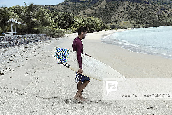Junger Mann mit Surfbrett am Strand