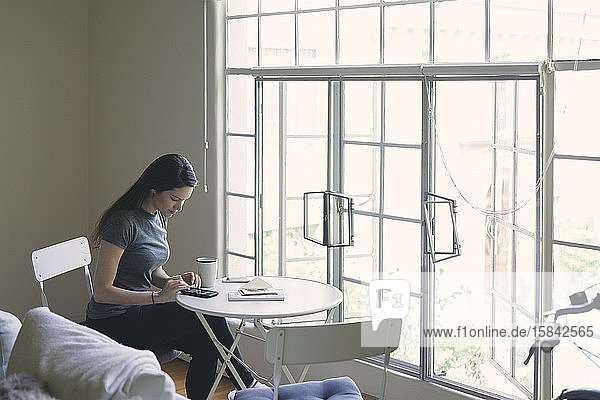 Textnachrichten von Frauen auf Smartphones  während sie am Tisch am Fenster im Wohnzimmer sitzen