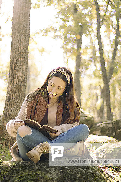 Junge Frau liest sitzend und umgeben von einem Wald ein Buch
