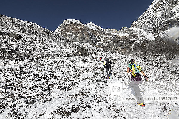Women climbers ascend a snowy hill below an imposing rock wall