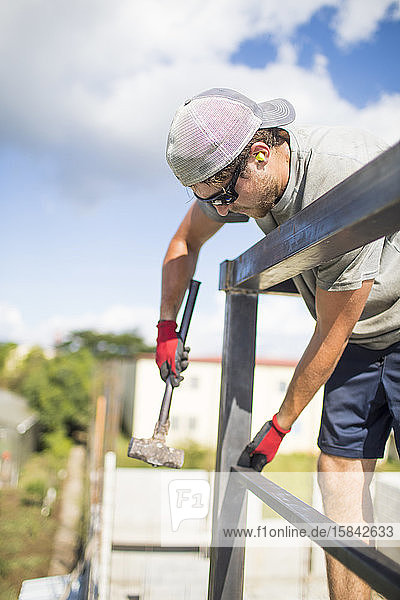 Bauarbeiter beim Bau eines Stahlgeländers auf dem Dach mit einem Hammer.