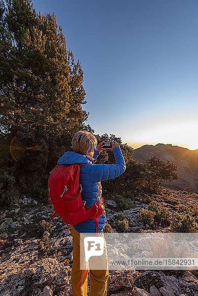 Woman hiking and taking a picture of the Puig Campana mountains.