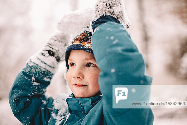Glücklicher Junge spielt im Winter mit Schnee