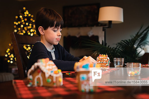 Young boy decorating gingerbread house with candy at Christmas.