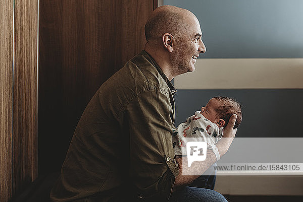 Seitenansicht eines glücklichen Vaters  der seinen neugeborenen Sohn im Krankenhaus hält
